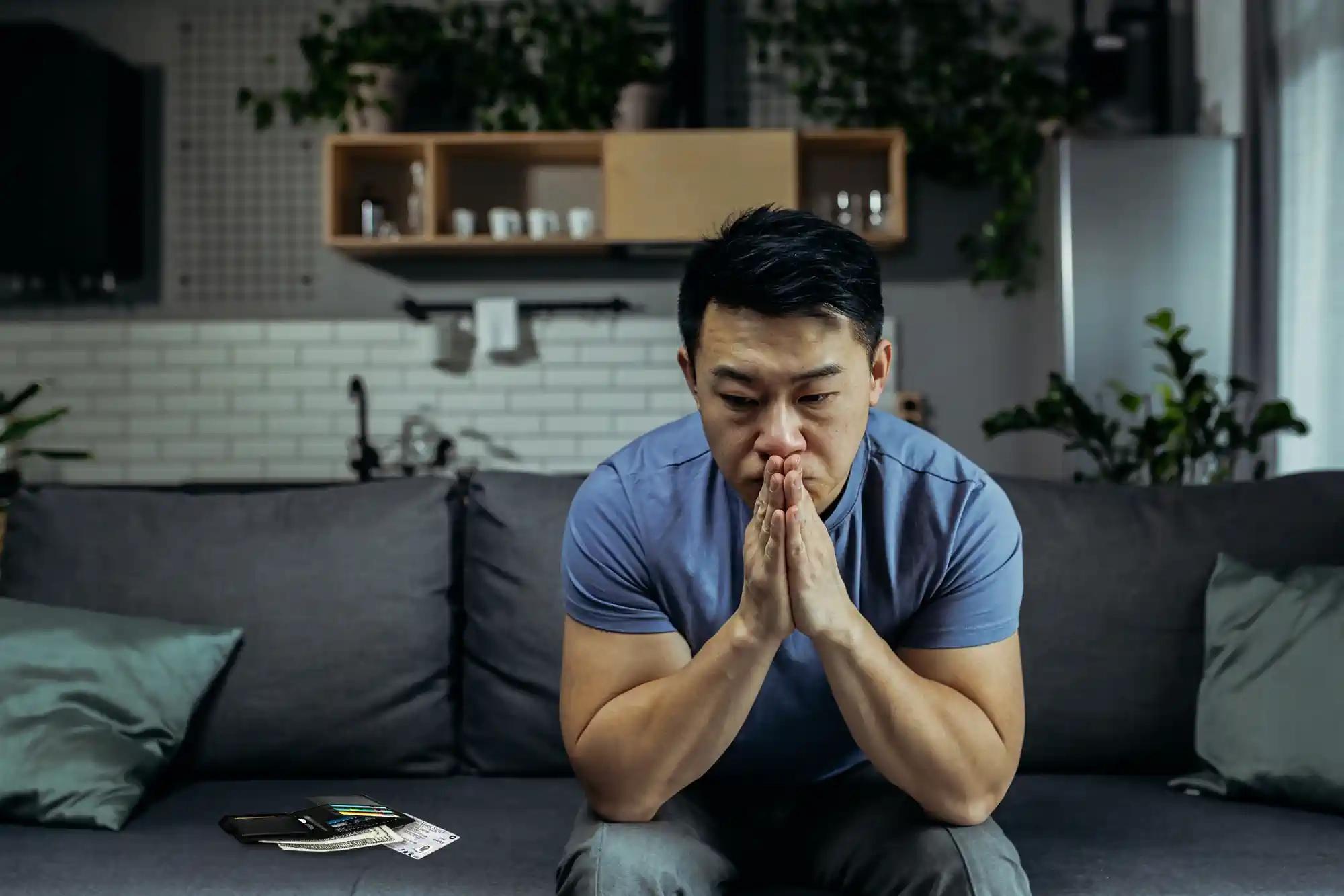 A worried Vietnamese man sits on the couch