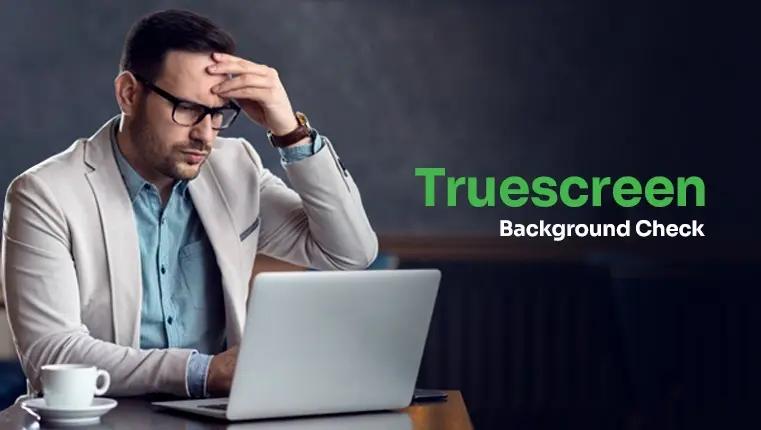 man holding his head sitting near laptop