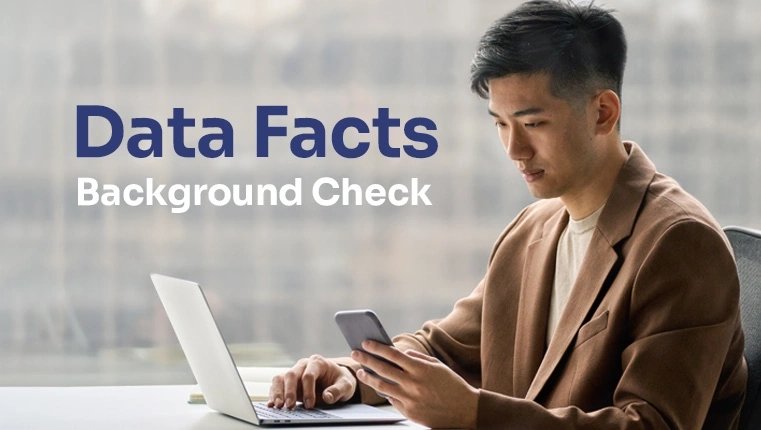 data facts background check a man sits at a table with one hand on a laptop and the other hand holds a phone