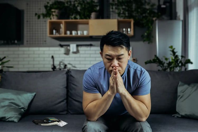 A worried Vietnamese man sits on the couch